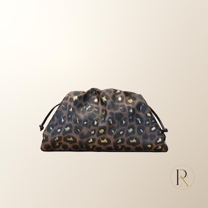 May include: A brown and black leopard print clutch bag with a gathered, pouch-like silhouette. The bag features a drawstring closure with thin black cords on each side and gold-colored accents scattered throughout the animal print pattern.