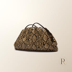 May include: A structured clutch bag featuring a tan and black snakeskin pattern with a gathered, ruched top design. The bag includes thin black handles and a soft, rounded silhouette, showcasing a detailed reptilian texture across the exterior.