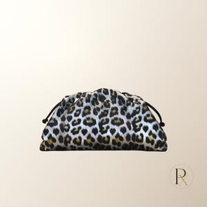 May include: A pouch-style clutch bag featuring a black, white, and tan leopard print pattern. The bag has a gathered, ruched top opening with thin black drawstring cords extending from each side, creating a soft, rounded, and voluminous silhouette.