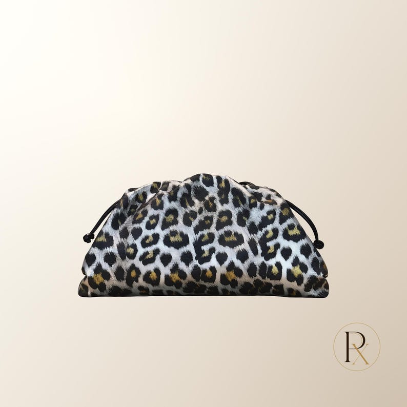 May include: A pouch-style clutch bag featuring a black, white, and tan leopard print pattern. The bag has a gathered, ruched top opening with thin black drawstring cords extending from each side, creating a soft, rounded, and voluminous silhouette.