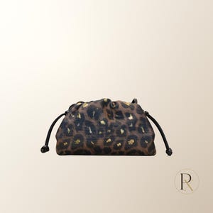 May include: A small drawstring pouch featuring a brown and black leopard print pattern with metallic gold accents. The bag has a soft, gathered top closure with thin black cords extending from each side, finished with small knotted ends.