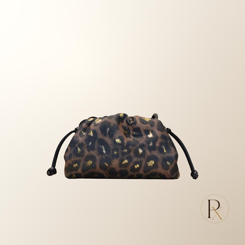 May include: A small drawstring pouch featuring a brown and black leopard print pattern with metallic gold accents. The bag has a soft, gathered top closure with thin black cords extending from each side, finished with small knotted ends.