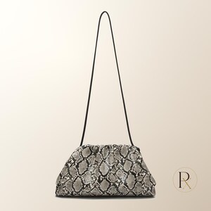 May include: A structured pouch handbag featuring a grey and black snakeskin pattern. The bag has a gathered, rounded top opening and a thin, long black shoulder strap. The design is compact with a textured surface and a soft, slouchy silhouette.