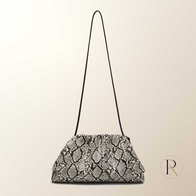 May include: A structured pouch handbag featuring a grey and black snakeskin pattern. The bag has a gathered, rounded top opening and a thin, long black shoulder strap. The design is compact with a textured surface and a soft, slouchy silhouette.