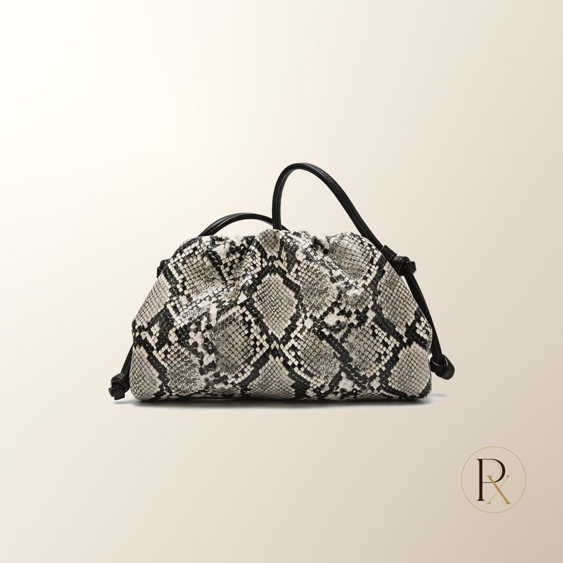 May include: A small, soft-structured pouch bag featuring a black and white snakeskin pattern. The bag has a gathered, ruched top opening and is equipped with a thin, black cord strap that is knotted at the sides for an adjustable carry style.