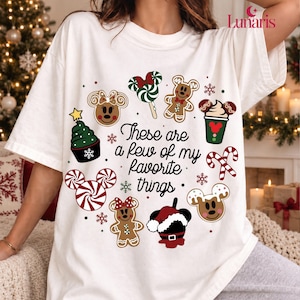 May include: A white short-sleeve t-shirt featuring a circular graphic of Christmas-themed icons including gingerbread cookies, candy canes, and a cupcake, with the text "These are a few of my favourite things" printed in black in the centre.