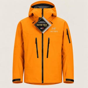 Op de afbeelding: Een feloranje jas met capuchon, voorzien van een zwarte ritssluiting over de gehele lengte, twee verticale borstzakken met zwarte ritsen en een kleinere zak met ritssluiting op de linkermouw. Een Gore-Tex productlabel is aan de voorzijde bevestigd.
