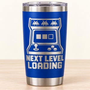 May include: A blue stainless steel tumbler with a silver laser-engraved graphic of a retro arcade cabinet featuring three alien figures at the top, a joystick, three buttons, and the text NEXT LEVEL LOADING printed in a bold, blocky font.