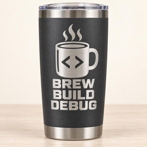 May include: A matte black stainless steel tumbler featuring a laser-engraved graphic of a coffee mug with a code bracket symbol on its side. Above the mug is a steam icon, and below it is the text "BREW BUILD DEBUG" in a bold, sans-serif font.