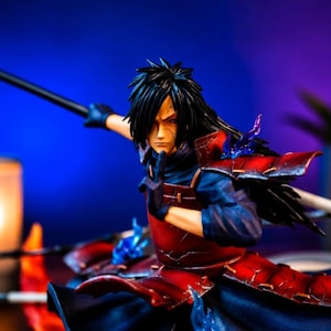 May include: A detailed anime character figurine featuring a figure with long black hair, wearing dark blue clothing and red segmented armor. The character is posed in a dynamic stance with one hand raised, accented by translucent blue flame effects.