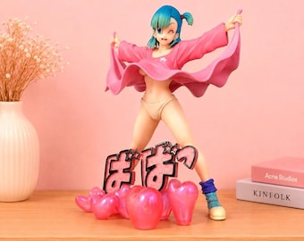May include: A plastic anime-style figurine of a character with blue hair, wearing a pink open shirt and beige underwear. The figure stands on a base decorated with pink heart shapes and Japanese text. The character has one eye closed in a wink.