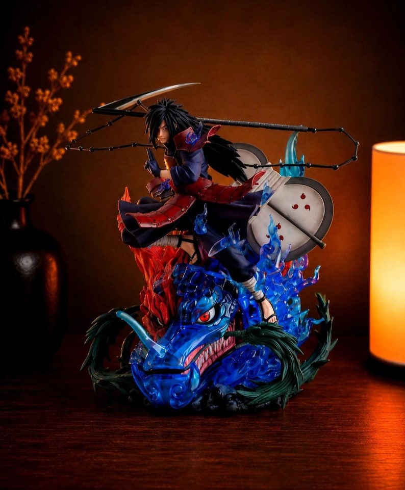 May include: A detailed anime character figurine featuring a dark-haired warrior in red and blue armor, wielding a large scythe and a circular fan with red markings. The figure stands atop a translucent blue dragon head surrounded by blue flames.