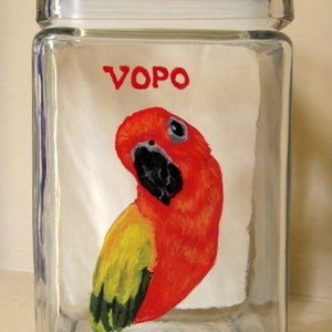 May include: A clear glass jar with a white lid, featuring a hand-painted red and yellow parrot with black eyes. The word "VOPO" is written in red on the front of the jar.