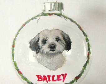Puede incluir: Un adorno navideño de vidrio transparente con un retrato pintado a mano de un perro blanco con orejas negras. El nombre del perro, "Bailey", está escrito en letras rosas en el adorno. El adorno está decorado con un borde de acebo verde.