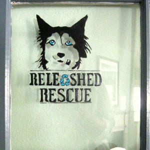 May include: A black and white illustration of a dog's head with blue eyes. The text "RELEASHED RESCUE" is below the image.