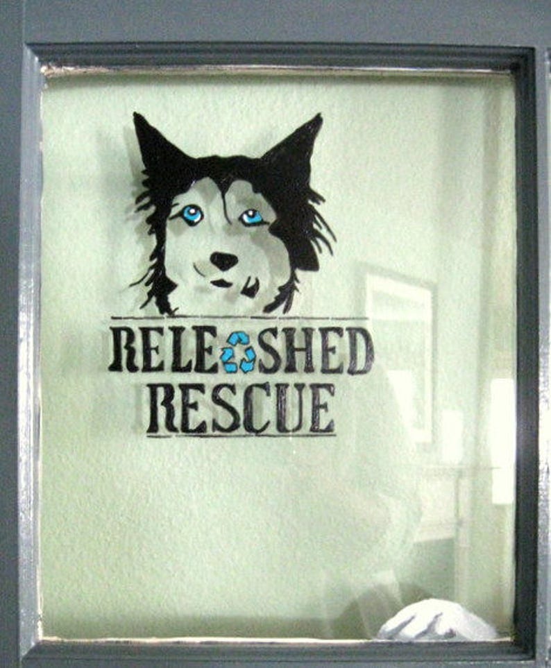May include: A black and white illustration of a dog's head with blue eyes. The text "RELEASHED RESCUE" is below the image.