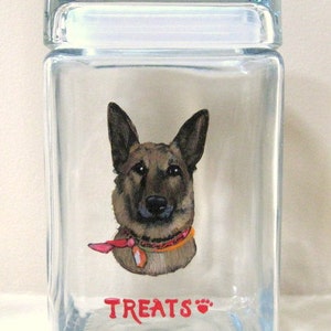 May include: A clear glass jar with a lid, featuring a hand-painted portrait of a German Shepherd dog wearing a red bandana. The jar has the word "TREATS" written in red with a paw print.