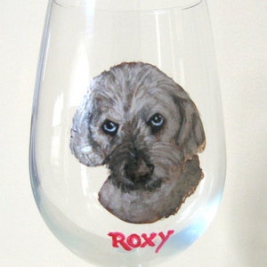 Puede incluir: Una copa de vino de vidrio transparente con un retrato pintado a mano de un perro gris con el nombre "ROXY" escrito en rojo debajo del perro.