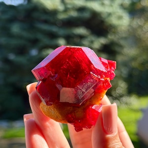 May include: A vibrant, deep red crystalline mineral specimen featuring sharp, geometric facets and a translucent, glass-like texture. The cluster displays a rich crimson hue with a solid, textured base, showcasing natural mineral formation and structure.