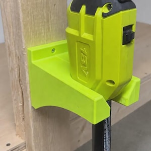 May include: A lime green 3D-printed wall mount bracket secured to a wooden post, holding a lime green 18V power tool. The bracket features a flat back plate with screw holes and a protruding cradle designed to support the base of the power tool.