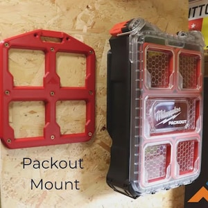 May include: A red plastic mounting plate with four square openings and a black and red Milwaukee Packout organiser case with a clear lid featuring a honeycomb pattern. The case has the text Milwaukee Packout printed on the front centre.