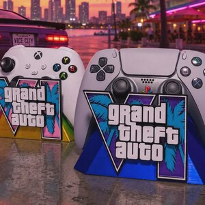 May include: A white Xbox controller and a white PlayStation 5 controller, each resting on a custom stand featuring the Grand Theft Auto VI logo with palm tree graphics. The stands are yellow and blue, set against a backdrop of a purple sports car.