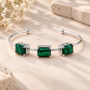 May include: A silver-toned open cuff bracelet featuring three rectangular malachite stones. Each stone is set in a silver-coloured metal frame with a polished finish. The bracelet has a smooth, curved band that terminates in small, rounded silver-toned ends.