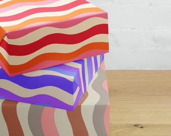 May include: Three rectangular boxes stacked vertically, each wrapped in paper with distinct wavy patterns. The top box features red, orange, pink, and cream waves. The middle box has purple, blue, and cream waves. The bottom box displays pink, brown, and gray waves.