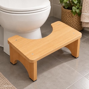 May include: A light wood-toned bathroom toilet stool featuring a U-shaped cutout design, four sturdy legs with black non-slip pads, and visible metal screws on the top surface. The word Oakvela is printed in the bottom left corner.