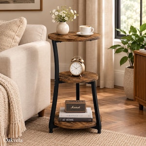 May include: A three-tier round side table with a dark wood grain finish and a black metal frame. The top shelf holds a white vase with flowers and a white coffee cup. The middle shelf holds a round analog clock. The bottom shelf holds books.