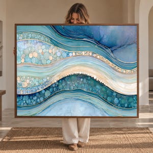 May include: A rectangular wall art piece featuring an abstract fluid design with layered waves of blue, teal, and cream colors. The composition includes circular bubble-like patterns and thin, metallic gold lines that define the flowing shapes.