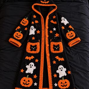 May include: A black crochet hooded cardigan featuring orange trim and buttons. The garment is decorated with appliqués of orange jack-o'-lanterns, white ghosts, black cats on the pockets, orange bats, and small white and orange stars.