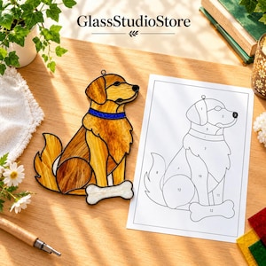 May include: A stained glass suncatcher shaped like a golden retriever dog with a blue collar and a white bone, accompanied by a numbered paper pattern template. The dog figure features amber and gold glass pieces joined by black metal solder lines.