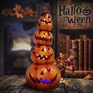 May include: A vertical stack of four orange jack-o'-lanterns with carved faces, featuring a small black top hat on the uppermost pumpkin. The pumpkins have glowing cutouts for eyes and jagged mouths, creating a tiered Halloween decoration.