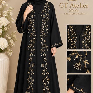 May include: A black abaya featuring gold floral embroidery along the front panels and sleeve cuffs. The garment includes a matching black hijab. The text GT Atelier Studio Premium Abaya is visible in the upper right corner of the image.