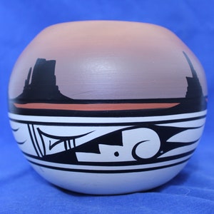 May include: A hand-painted ceramic pot with a black, white, and red geometric design. The pot features a landscape scene with a sunset and mountains in the background.