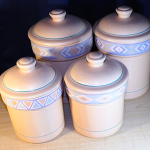 May include: Set of four ceramic canisters with lids. The canisters are beige with blue and pink geometric designs. The lids are beige with a blue trim.
