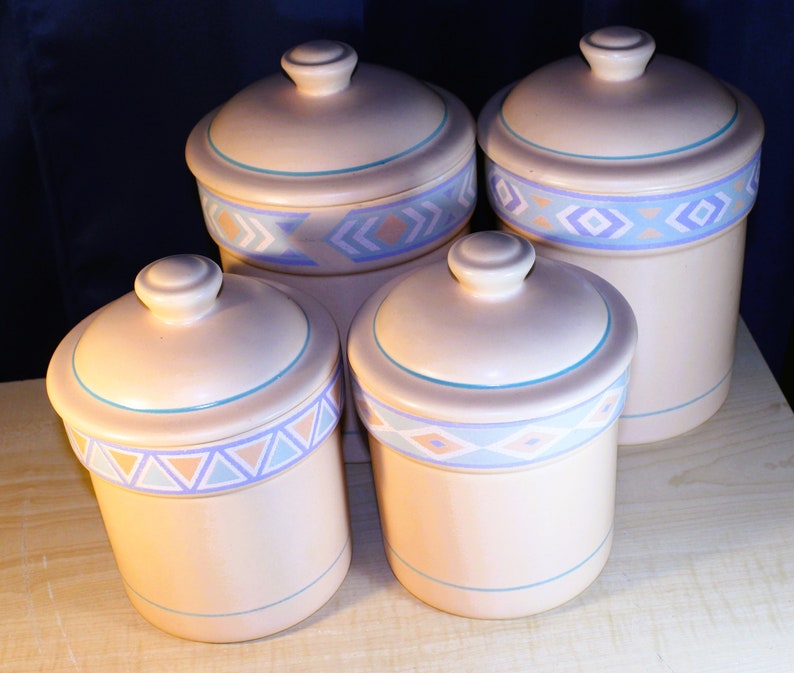 May include: Set of four ceramic canisters with lids. The canisters are beige with blue and pink geometric designs. The lids are beige with a blue trim.