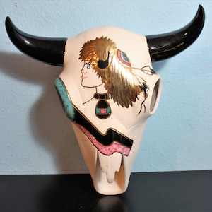 May include: White ceramic buffalo skull with black horns and a painted design of a Native American woman wearing a headdress with gold accents.
