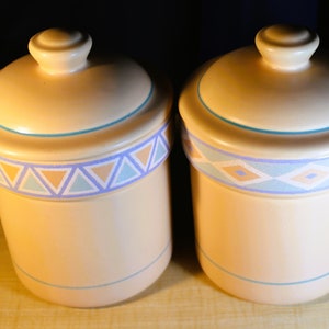 May include: Two ceramic canisters with lids, featuring a Southwestern-inspired design. The canisters are beige with blue, orange, and white geometric patterns.