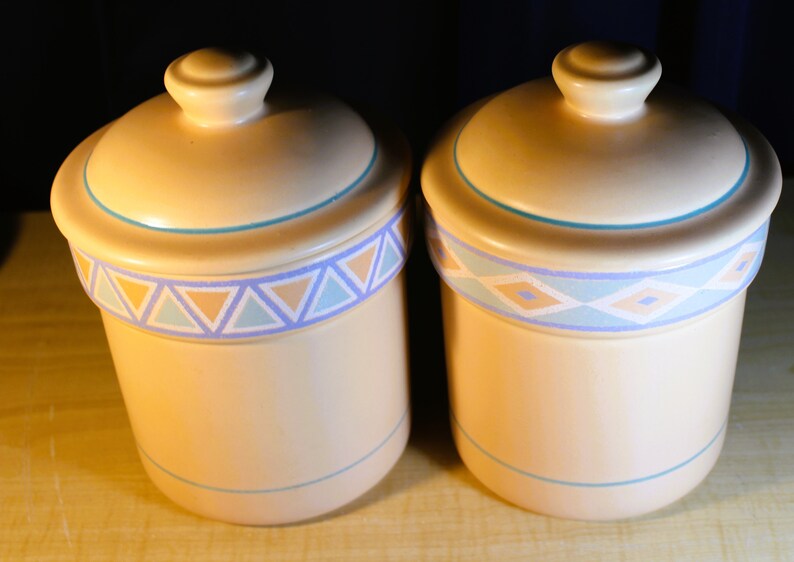 May include: Two ceramic canisters with lids, featuring a Southwestern-inspired design. The canisters are beige with blue, orange, and white geometric patterns.