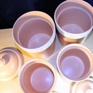 May include: Set of five ceramic canisters with lids. The canisters are a light brown colour with a white and blue design around the top edge. The lids are a light brown colour with a smooth surface.