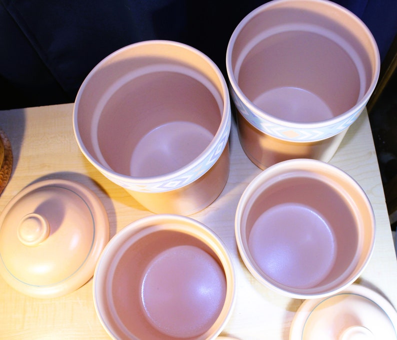 May include: Set of five ceramic canisters with lids. The canisters are a light brown colour with a white and blue design around the top edge. The lids are a light brown colour with a smooth surface.