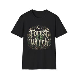 Op de afbeelding: Een zwart t-shirt met korte mouwen en een cirkelvormige afbeelding met de tekst Forest Witch in een decoratief lettertype. Het ontwerp bevat een silhouet van een heks, een maansikkel, sterren, paddenstoelen en verstrengelde bosranken.