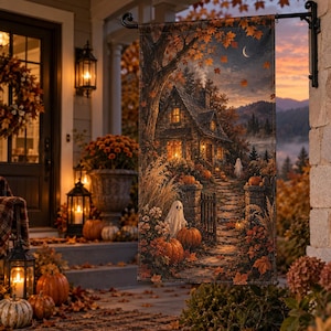 Puede incluir: Una bandera de jardín rectangular con una ilustración detallada de una casa de piedra al atardecer durante el otoño. La escena incluye calabazas naranjas, hierbas altas y dos pequeñas figuras de fantasmas en un camino de piedra.