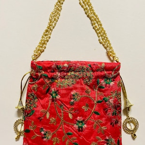 May include: A red drawstring bag with a floral pattern and gold embellishments. The bag has a long gold chain strap with white beads.