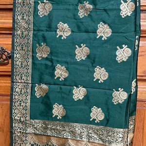 May include: Emerald green fabric with gold floral and patterned accents. The fabric features repeating gold floral motifs and a decorative border with figures. This textile is likely used for clothing or home decor.