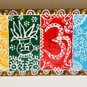 May include: A wooden box with four painted panels. Each panel features a different design in white on a colored background. The designs include a plant in a pot, the Om symbol, and two floral patterns. The box is decorated with a gold trim.