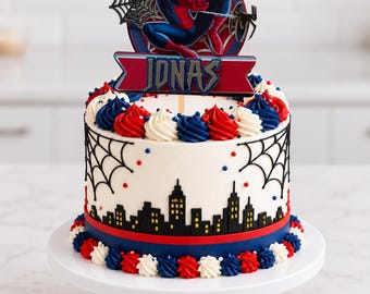 May include: A round cake with white frosting, decorated with a black city skyline silhouette, spider web piping, and red, white, and blue buttercream rosettes. A cake topper features Spider-Man, a city skyline, and the name JONAS.