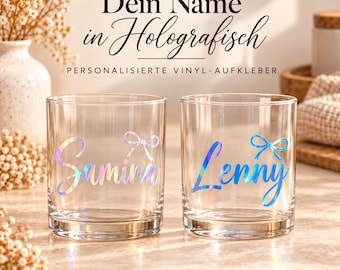 May include: Two clear glass tumblers featuring holographic vinyl decals. One glass displays the name Samina in cursive script with a small bow icon, and the other displays the name Lenny in cursive script with a small bow icon. Text reads Dein Name in Holografisch, PERSONALISIERTE VINYL-AUFKLEBER, and THE WILLIAMS EDIT.